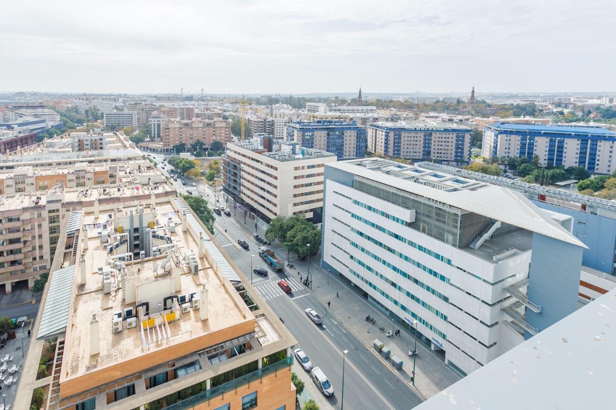 Vista de una amplia avenida de Nervión con palmeras, tráfico y edificios residenciales, reflejando el ambiente elegante al vender piso en Nervión.